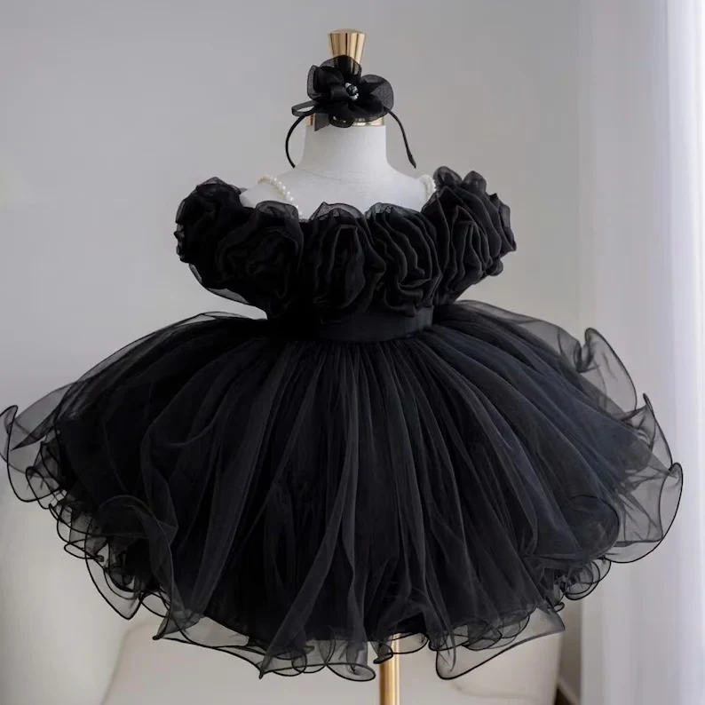 Black princess party dress for girls featuring large fabric flowers across the bodice, a matching floral headpiece, and a dramatic full tulle skirt.