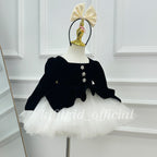Angled view of a girls black velvet princess dress with long sleeves, floral buttons and a white layered tulle skirt.