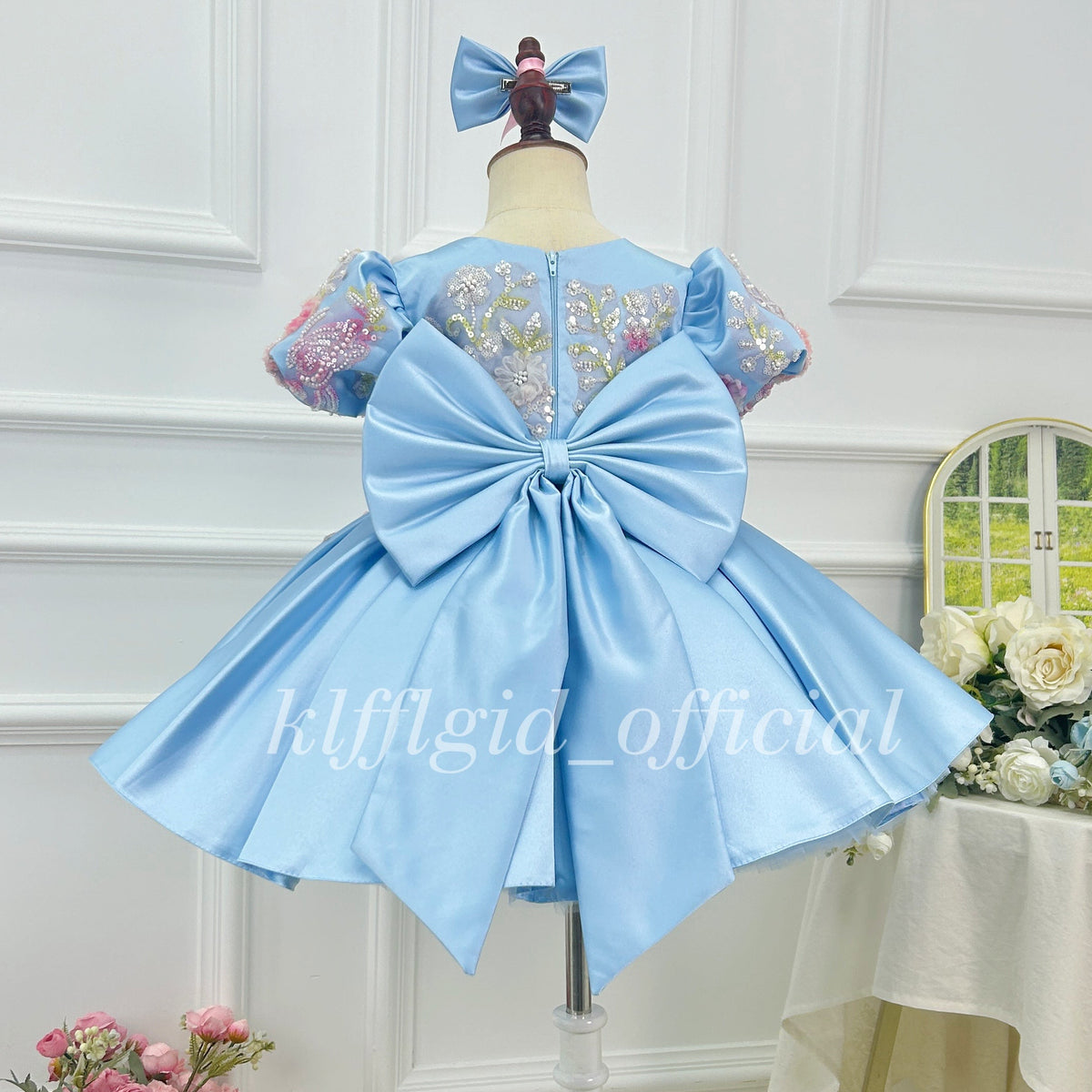 Back view of a light blue girls satin princess dress with oversized bow and floral embroidered sleeves
