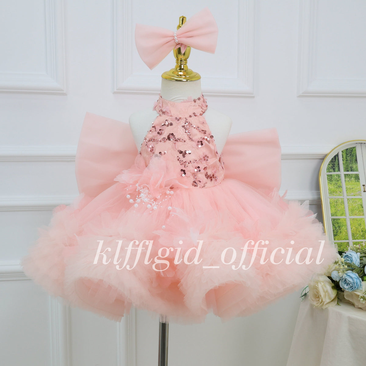 Close view of a blush pink girls' princess dress with sequin bodice details, floral waist embellishments, pearl accents, and a voluminous tulle skirt