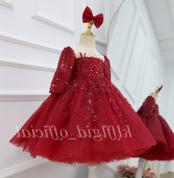 Angled view of a burgundy princess dress for girls with shimmering sequin details, long sleeves, a fitted bodice, and a full flared skirt.