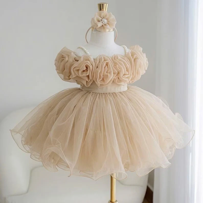 Champagne-colored flower girl dress for girls with large fabric flowers across the bodice, a matching headpiece, and a full tulle skirt.