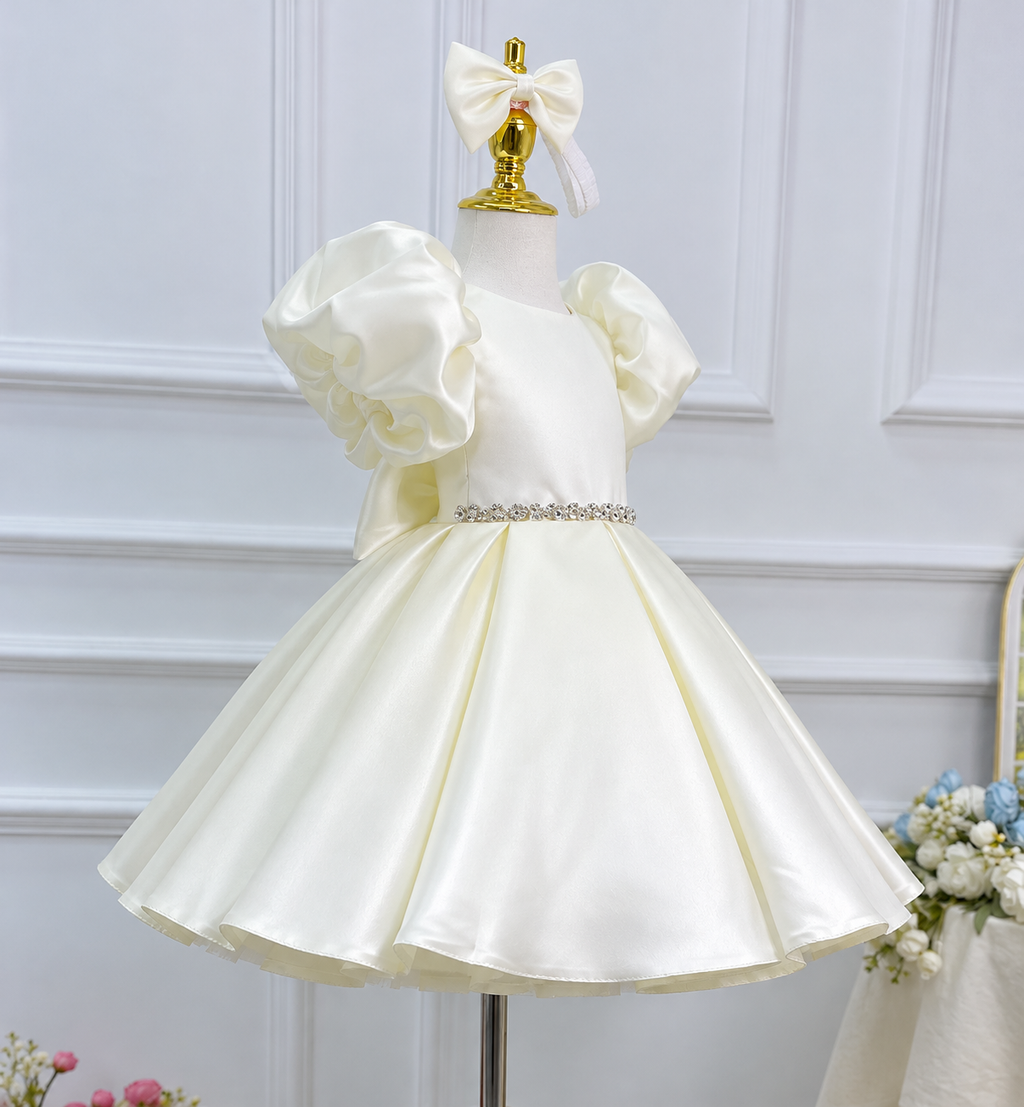 Angled view of an ivory satin princess gown with gathered puff sleeves, a sparkling waist embellishment, and a glossy full skirt