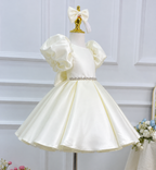 Angled view of an ivory satin princess gown with gathered puff sleeves, a sparkling waist embellishment, and a glossy full skirt