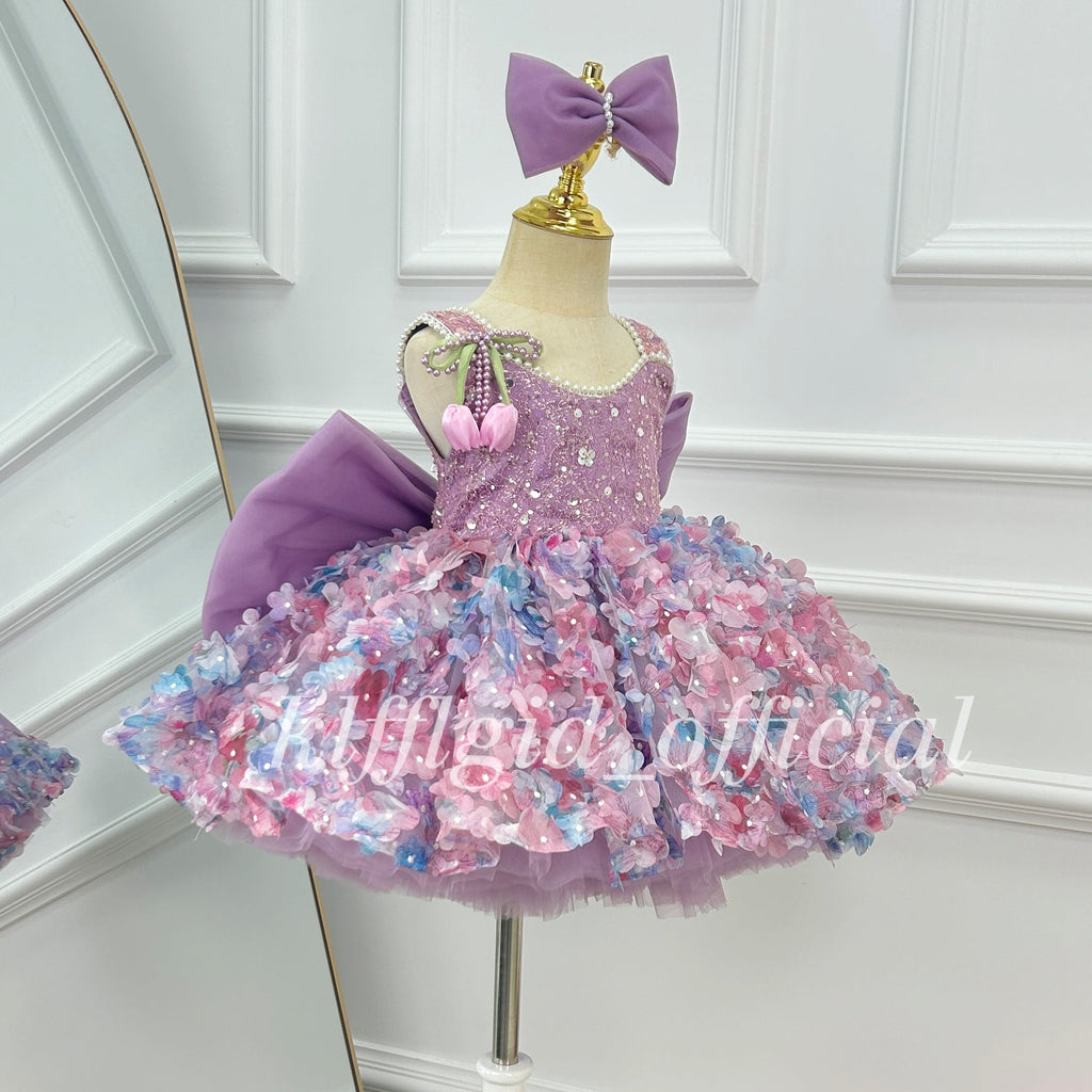 Side view of a lavender girls' party dress with a sparkling sleeveless bodice, colorful three-dimensional floral decorations, a full layered skirt, and a large purple bow.
