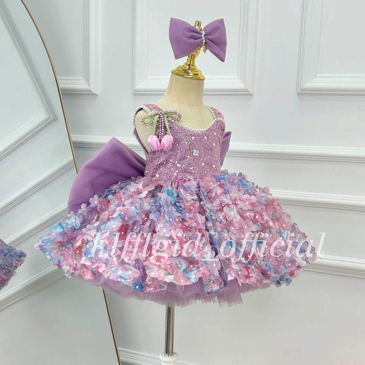 Side view of a lavender girls' party dress with a sparkling sleeveless bodice, colorful three-dimensional floral decorations, a full layered skirt, and a large purple bow.