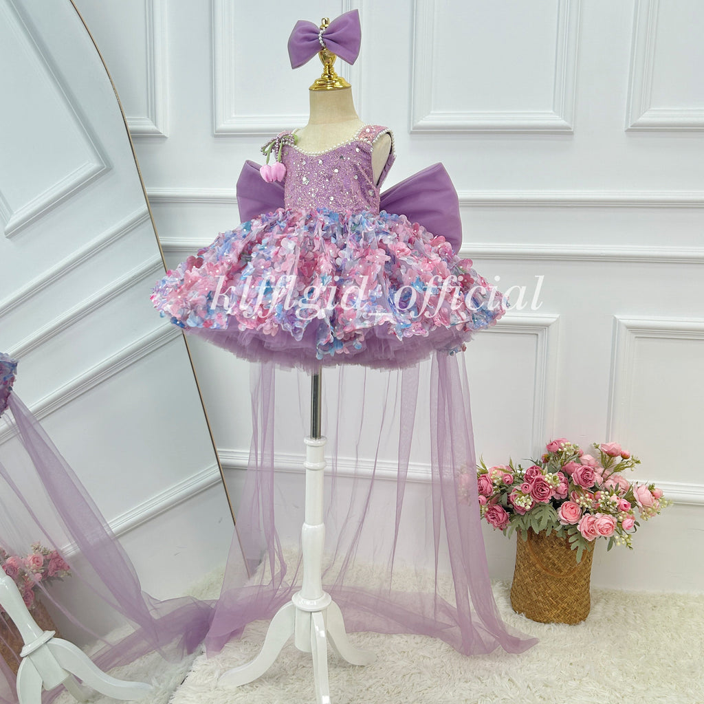 Angled view of a lavender girls' princess gown with a glittering bodice, pink and blue floral embellishments, a voluminous short skirt, and long sheer tulle panels.
