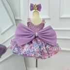 Close-up of the back of a lavender princess dress featuring an oversized purple bow with pearl-like center trim, a sparkling bodice, and colorful floral skirt decorations.