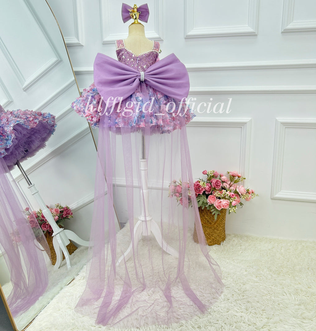 Back view of a lavender princess gown for girls with a large satin-look bow, sparkling embellished bodice, colorful floral skirt, and floor-length sheer tulle train.
