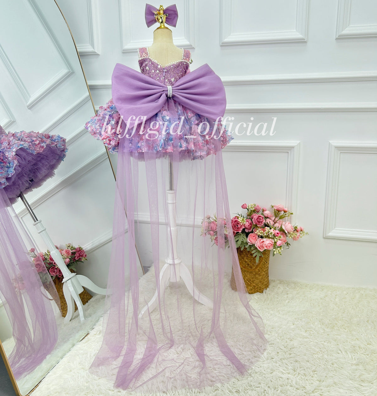 Back view of a lavender princess gown for girls with a large satin-look bow, sparkling embellished bodice, colorful floral skirt, and floor-length sheer tulle train.