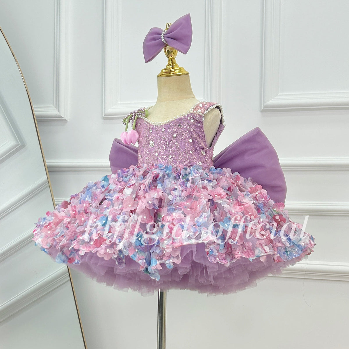 Three-quarter view of a lavender princess dress for girls featuring a glittering bodice, pink and blue floral skirt embellishments, and a voluminous layered silhouette.