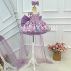 Three-quarter view of a lavender toddler princess gown featuring colorful floral skirt decorations, a sparkling bodice, an oversized back bow, and a flowing tulle train.
