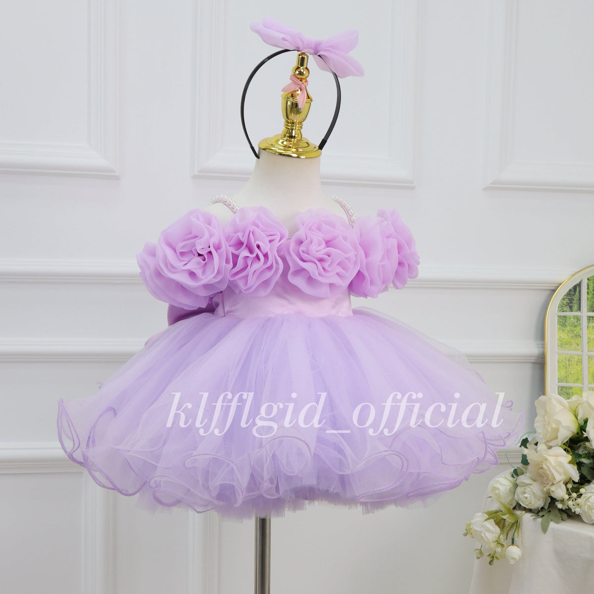 Three-quarter view of a lavender girls' birthday gown with oversized fabric flowers, a full flared skirt, and curled tulle edging.