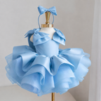 Light blue satin princess dress for girls with sculpted shoulder bows, dramatic layered ruffle skirt and matching blue bow headband, front view