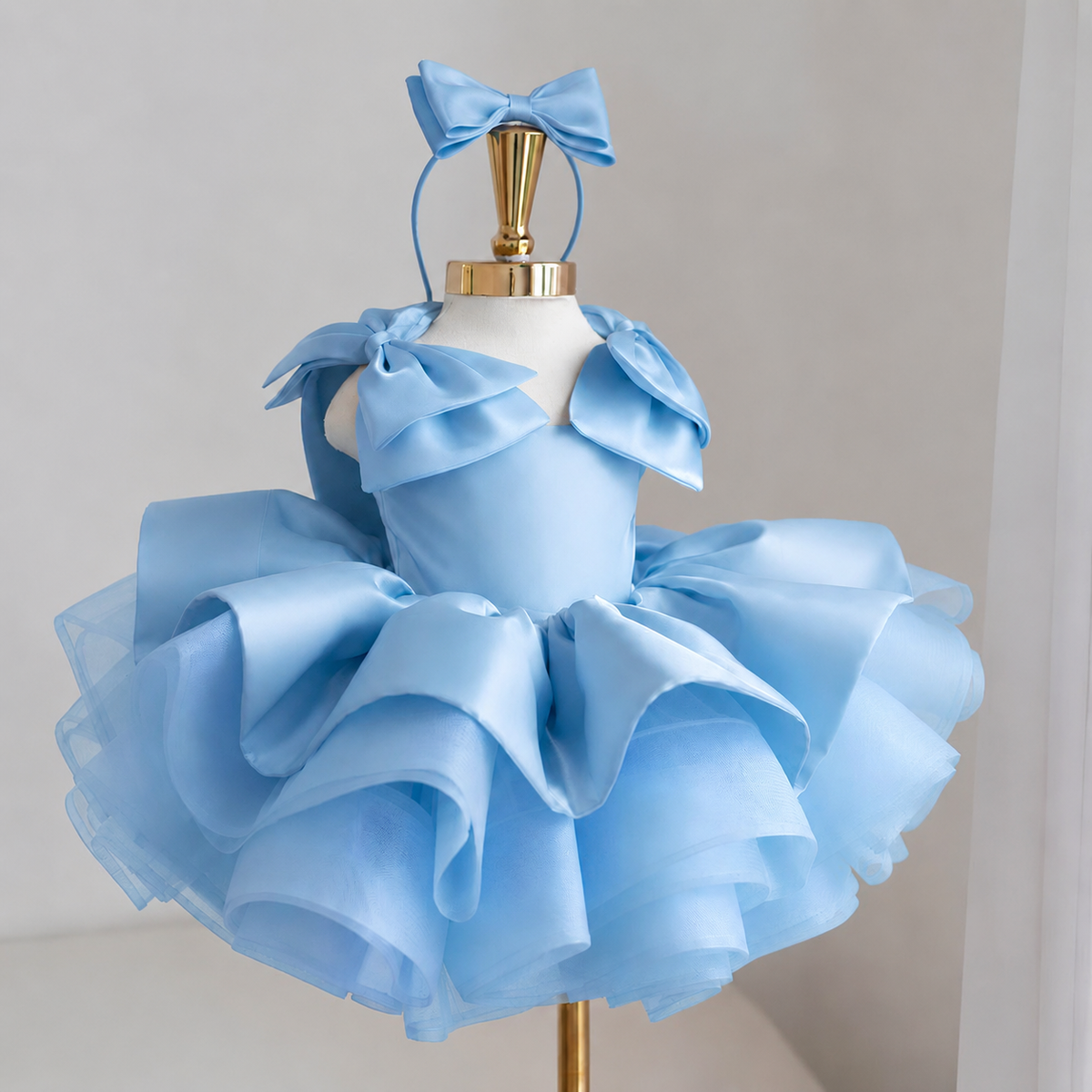 Light blue satin princess dress for girls with sculpted shoulder bows, dramatic layered ruffle skirt and matching blue bow headband, front view