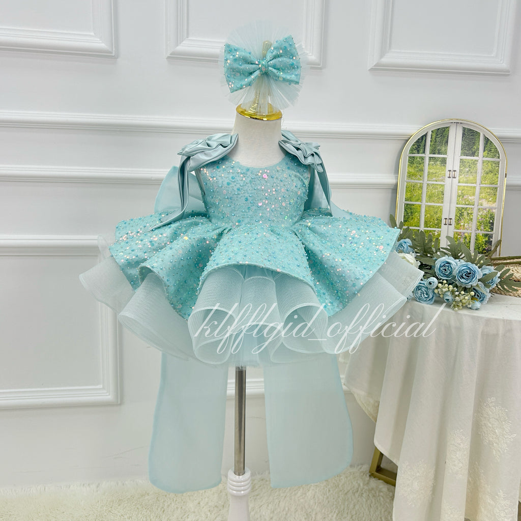 Front view of a light blue girls' sequin tulle princess dress with a sparkling bodice, layered flared skirt, shoulder ruffles, and matching bow headpiece.