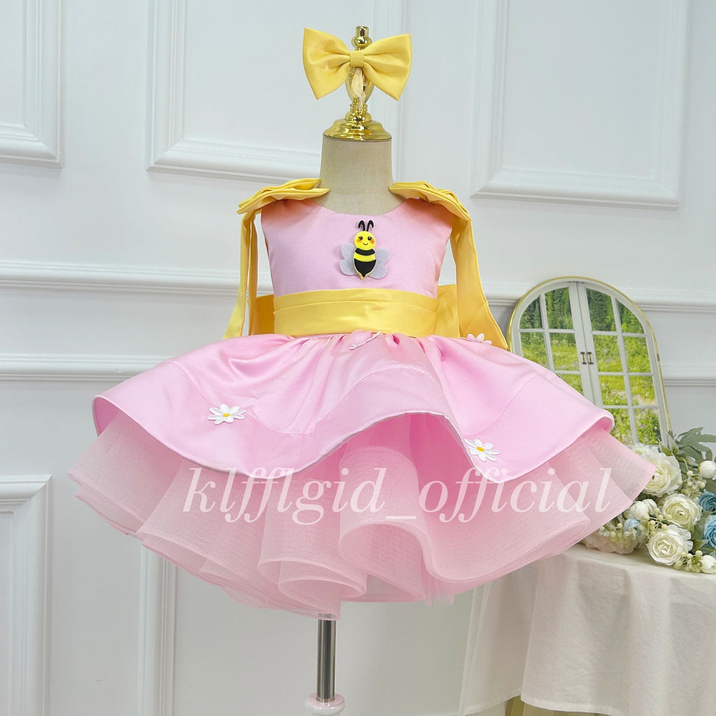 Front view of a pink girls' princess dress with a yellow waistband, bee appliqué on the bodice, daisy decorations, and a layered tulle skirt.