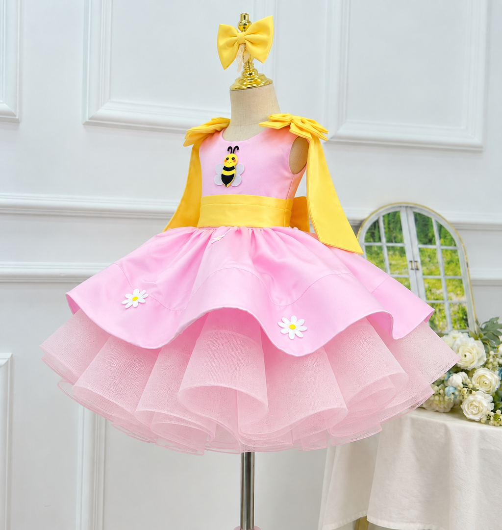 Angled front view of a pink tulle birthday dress for girls with a yellow waistband, bee bodice decoration, daisy embellishments, and multiple skirt layers.