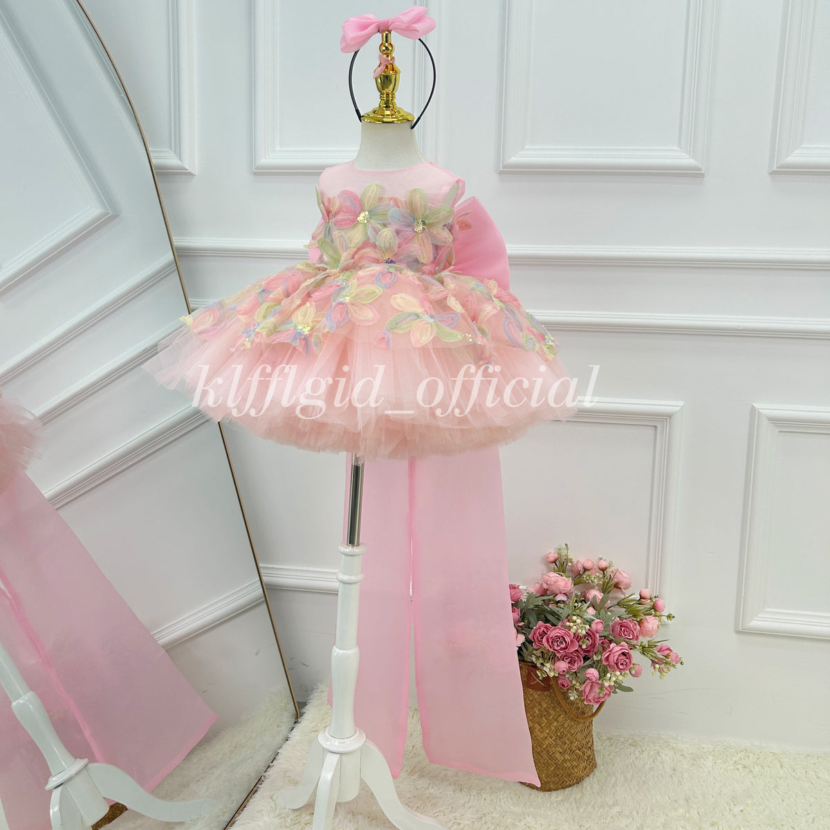 Pink floral flower girl dress shown at an angle with pastel flower embellishments, a full layered tulle skirt and a long pink train