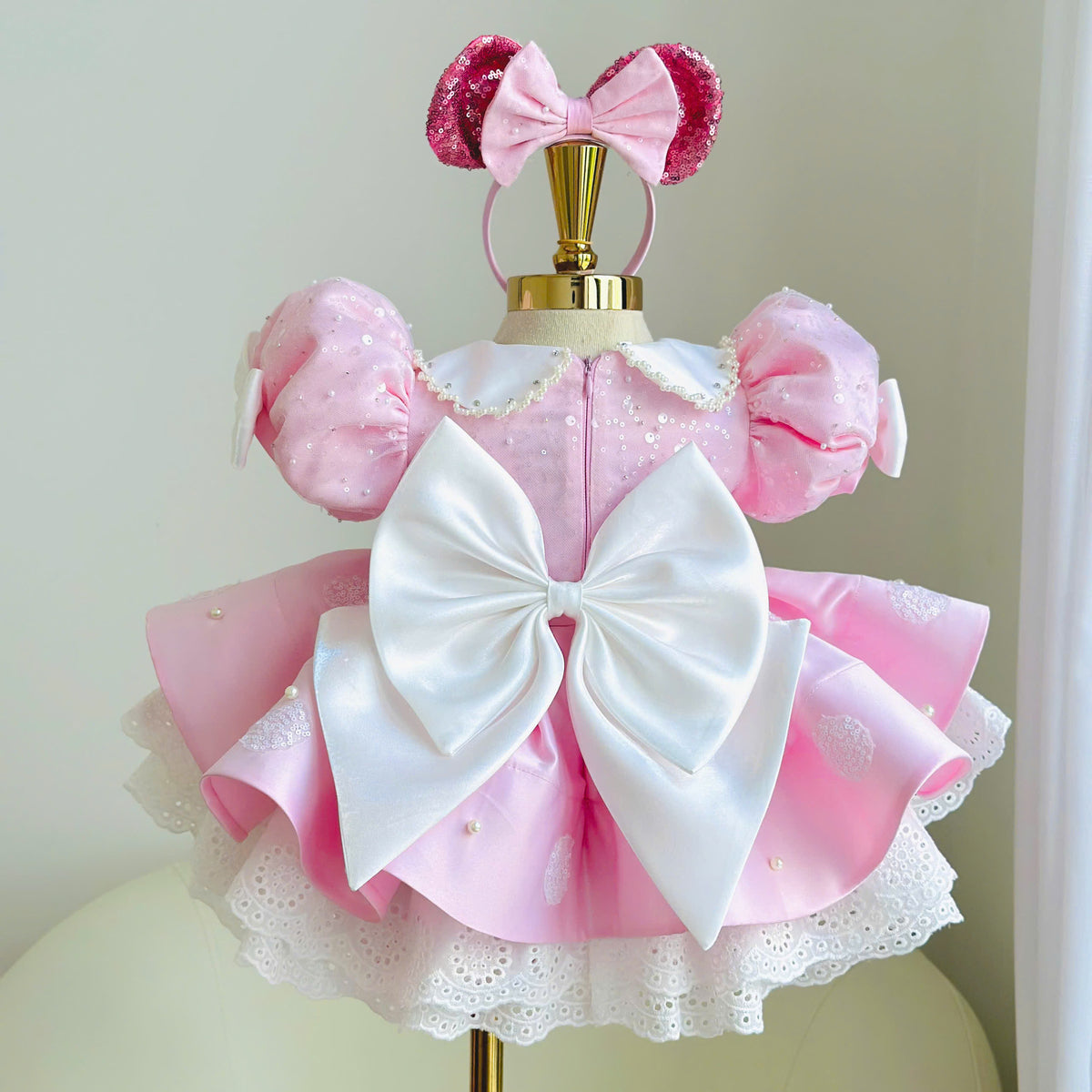 Back view of pink girls princess dress featuring a large white satin bow, puff sleeves, polka dot skirt and lace hem