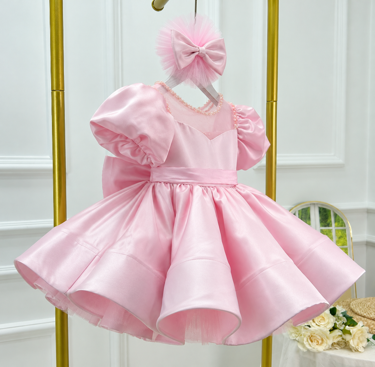 Angled view of a pink satin princess dress with voluminous puff sleeves, a sheer embellished neckline, a wide waistband, and a glossy flared skirt