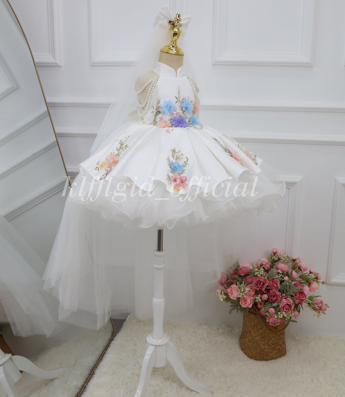 Side angle of a white girls princess dress with colorful floral appliques, pearl shoulder chains and layered tulle