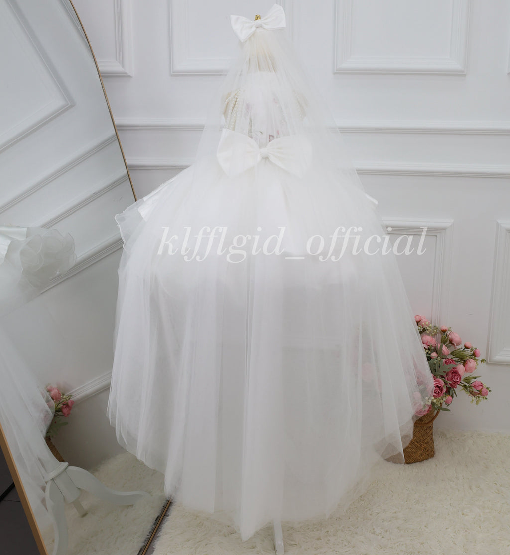Rear view of a white girls princess dress with a large white bow and floor-length sheer veil