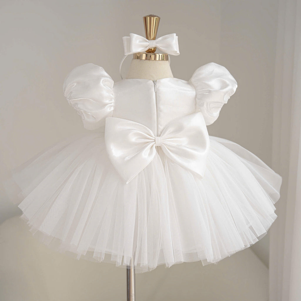 Back view of white girls princess dress with a large satin back bow, puff sleeves and a full layered tulle skirt