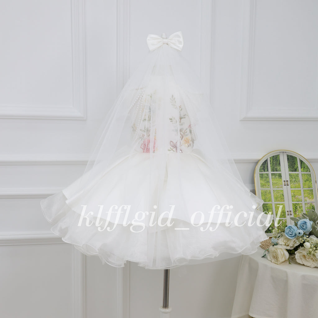 Back view of a white girls princess dress with a long sheer tulle veil and white bow