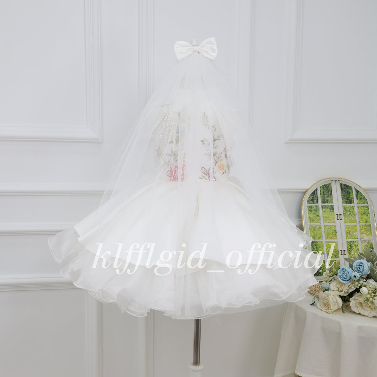 Back view of a white girls princess dress with a long sheer tulle veil and white bow