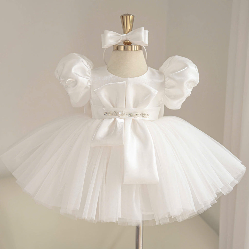 White satin princess dress for girls with puff sleeves, geometric bow bodice detail, jeweled waist belt and layered tulle skirt