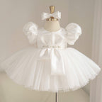 White satin princess dress for girls with puff sleeves, geometric bow bodice detail, jeweled waist belt and layered tulle skirt