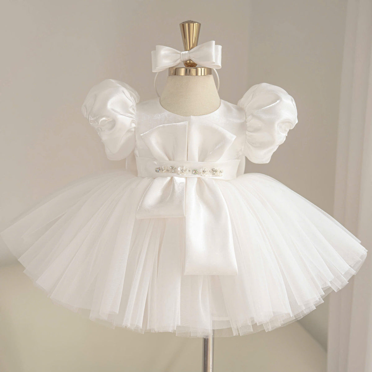 White satin princess dress for girls with puff sleeves, geometric bow bodice detail, jeweled waist belt and layered tulle skirt