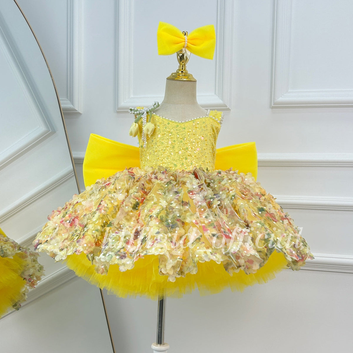 Yellow girls' princess dress featuring a sleeveless embellished bodice, multicolored floral skirt details, a full layered skirt, and a large matching yellow bow.