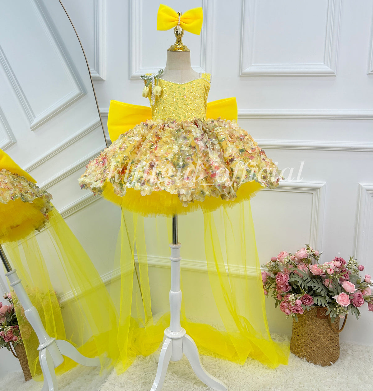 Front view of a yellow girls' princess gown with a sparkling bodice, multicolored floral skirt decorations, an oversized yellow bow, and a long sheer yellow tulle train.
