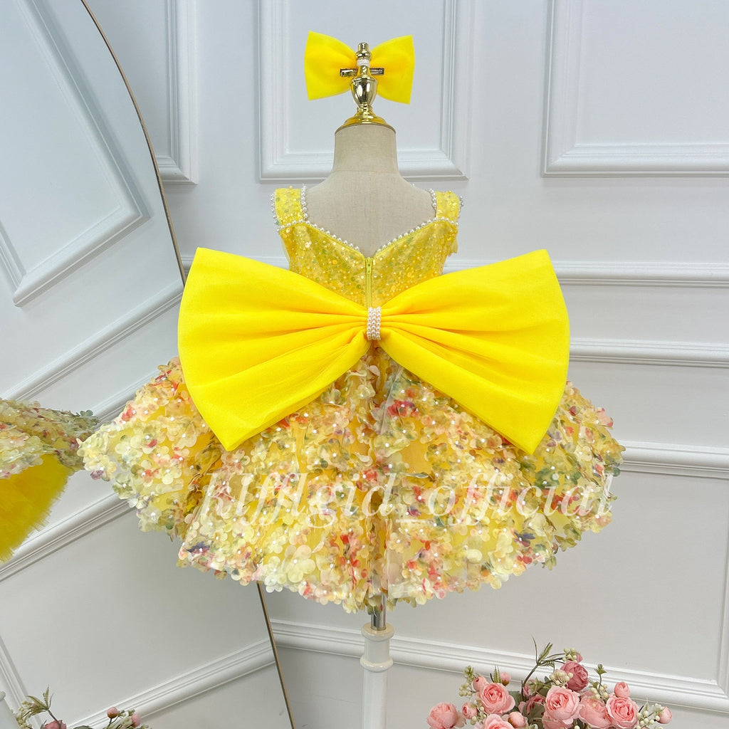 Back view of a yellow girls' princess dress with an oversized satin-look yellow bow, a sparkling bodice, and a full skirt decorated with multicolored floral details.